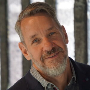 Chris Jennings smiles in front of a light grey background.